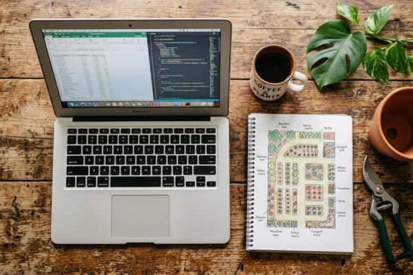 A clean modern workspace setup featuring a laptop alongside real physical gardening tools and notebooks.