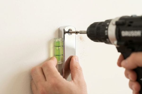 Hands using a spirit level and drilling chrome wall brackets into drywall